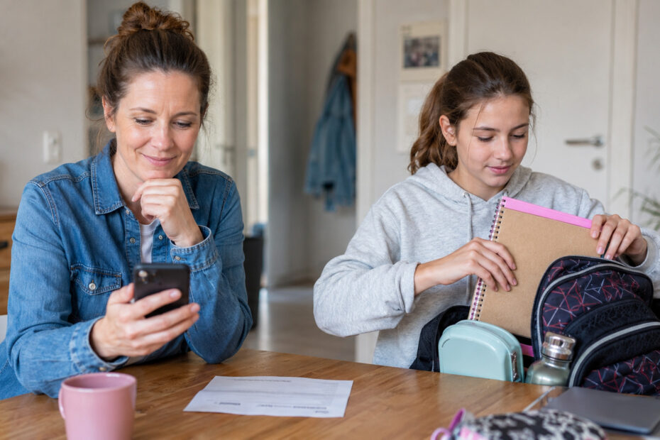 Mutter liest eine Nachricht zur Kindergelderhöhung 2028, während ihre Tochter den Schulrucksack packt