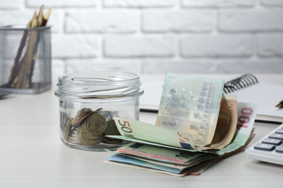 Ein Glas mit Münzen, Geldscheinen und ein Taschenrechner auf einem Tisch, symbolisch für Sonderbedarf beim Kindesunterhalt